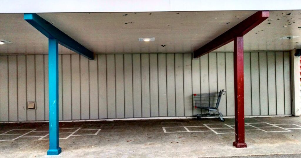 An empty shopping cart parked under a store overhang
