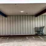 An empty shopping cart parked under a store overhang